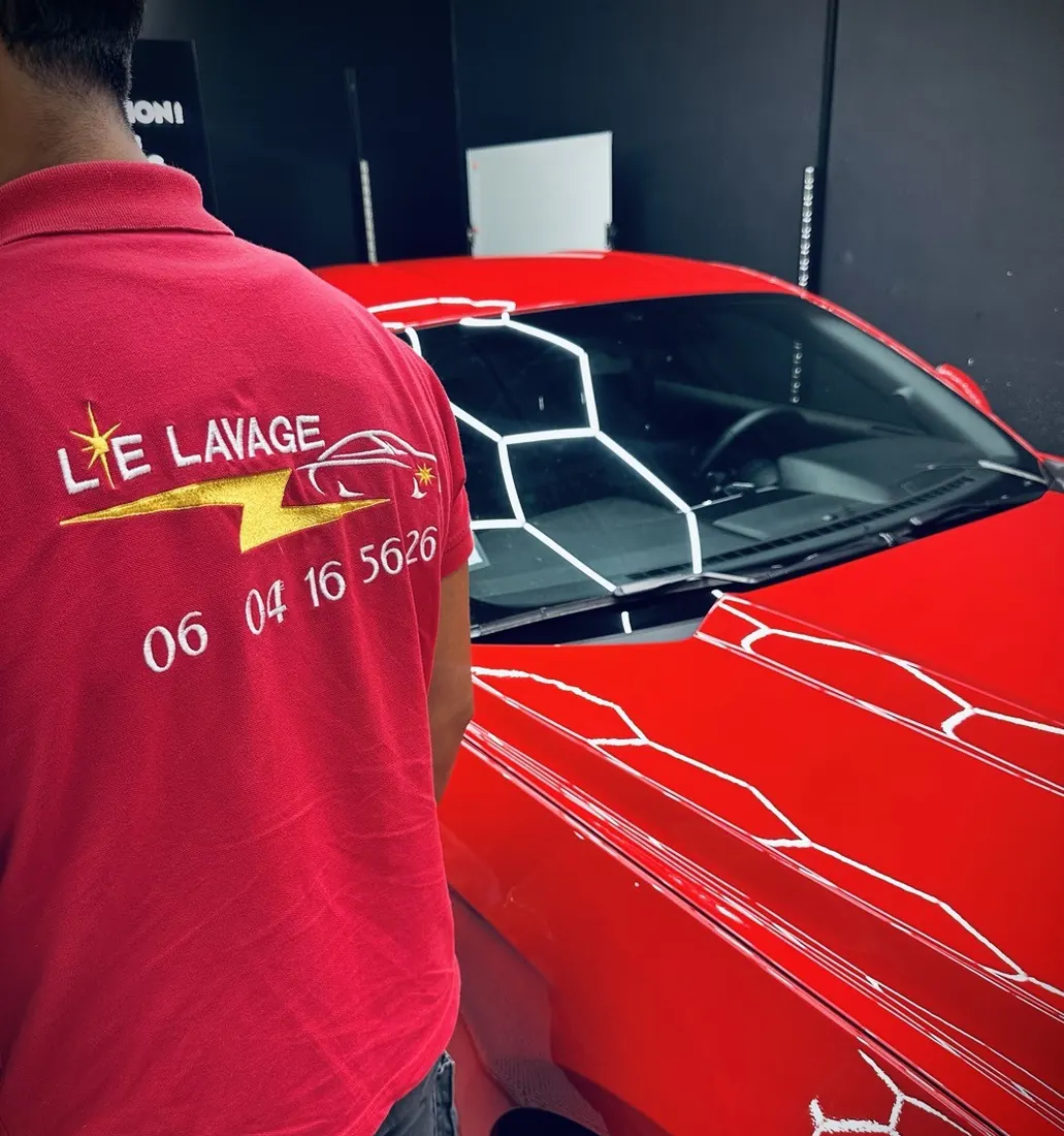 Dario Lalli en polo Le Lavage 89 devant une voiture rouge, sous une rampe d'éclairage de studio