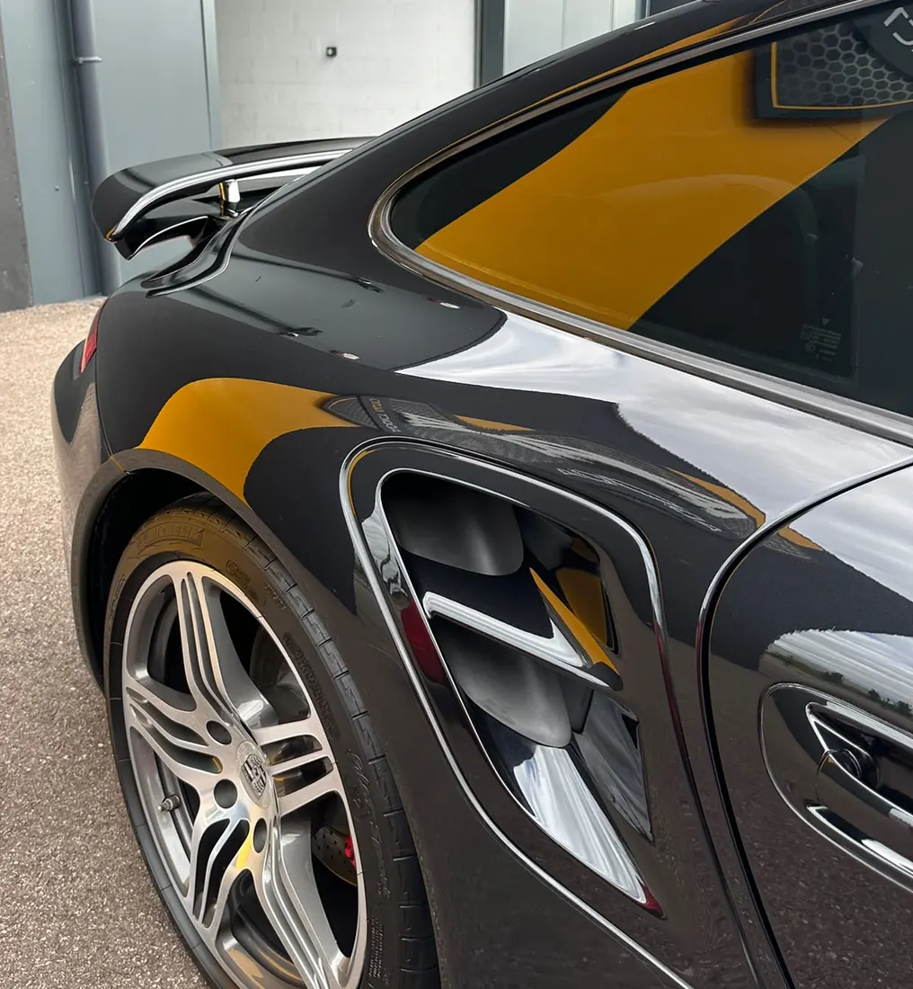 Aile arrière d'une Porsche noire reflétant le bâtiment voisin